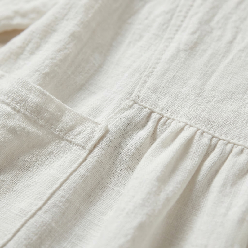 Close-up of the white linen fabric showing the pocket stitching and soft pleated waist detail.