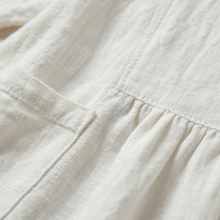 Close-up of the white linen fabric showing the pocket stitching and soft pleated waist detail.