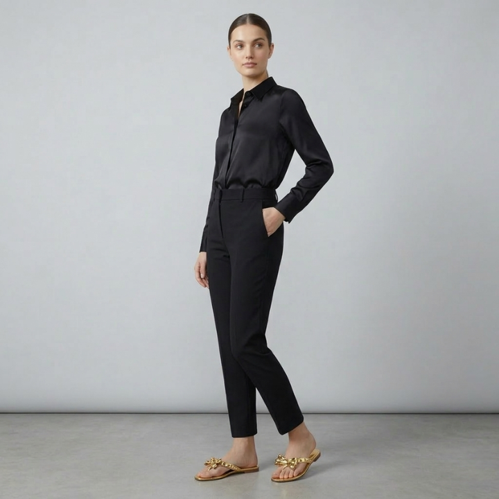 A female model posing in beige or nude-colored studded bow jelly flip flops and black trousers.