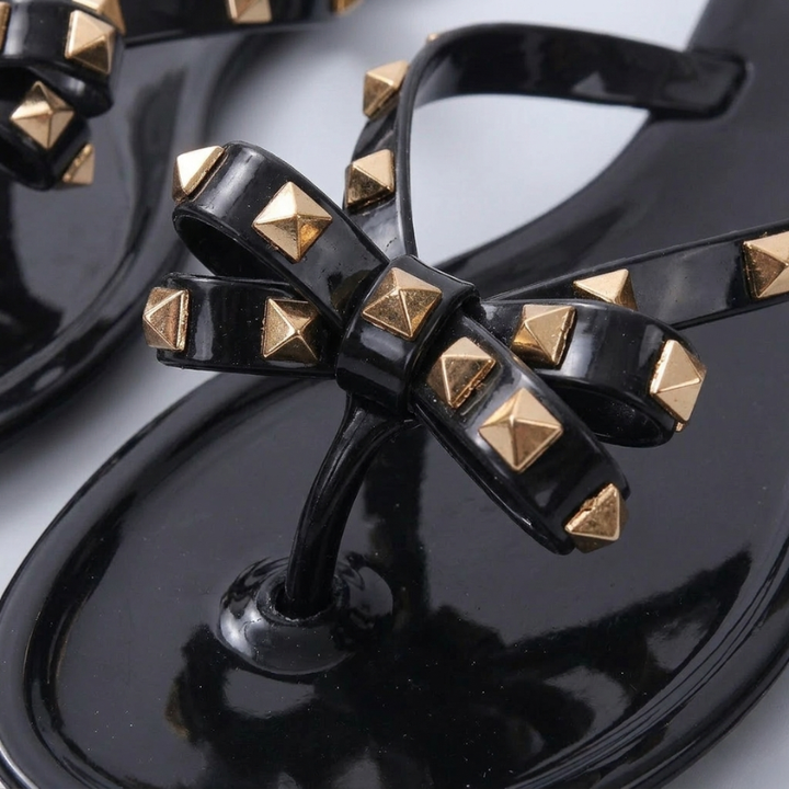 Extreme close-up of a black jelly sandal showing the metallic gold pyramid studs on a decorative bow strap.