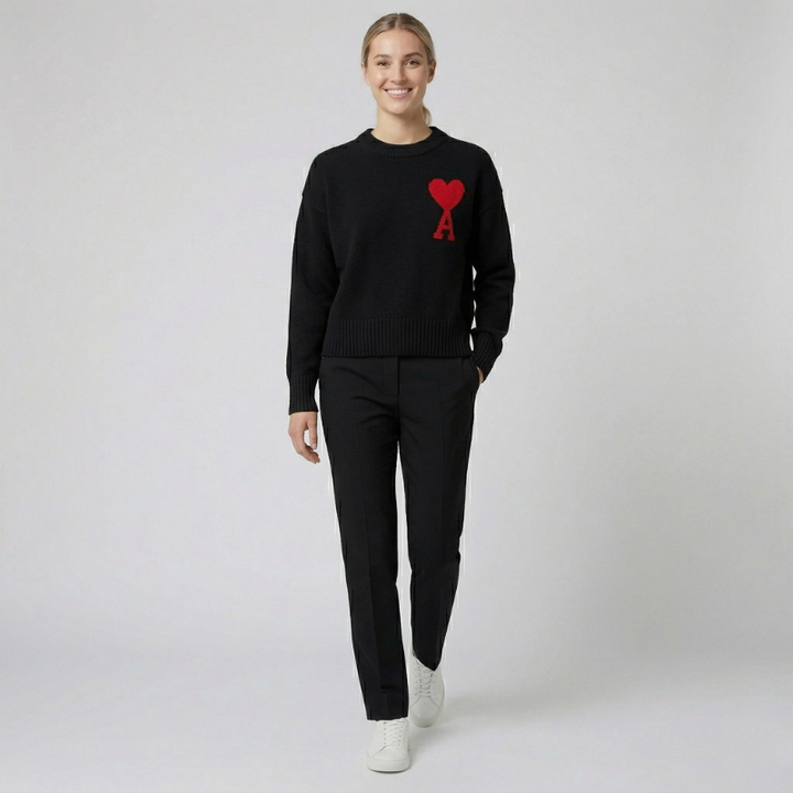 A woman wearing a classic black crewneck knit sweater with a red heart emblem.