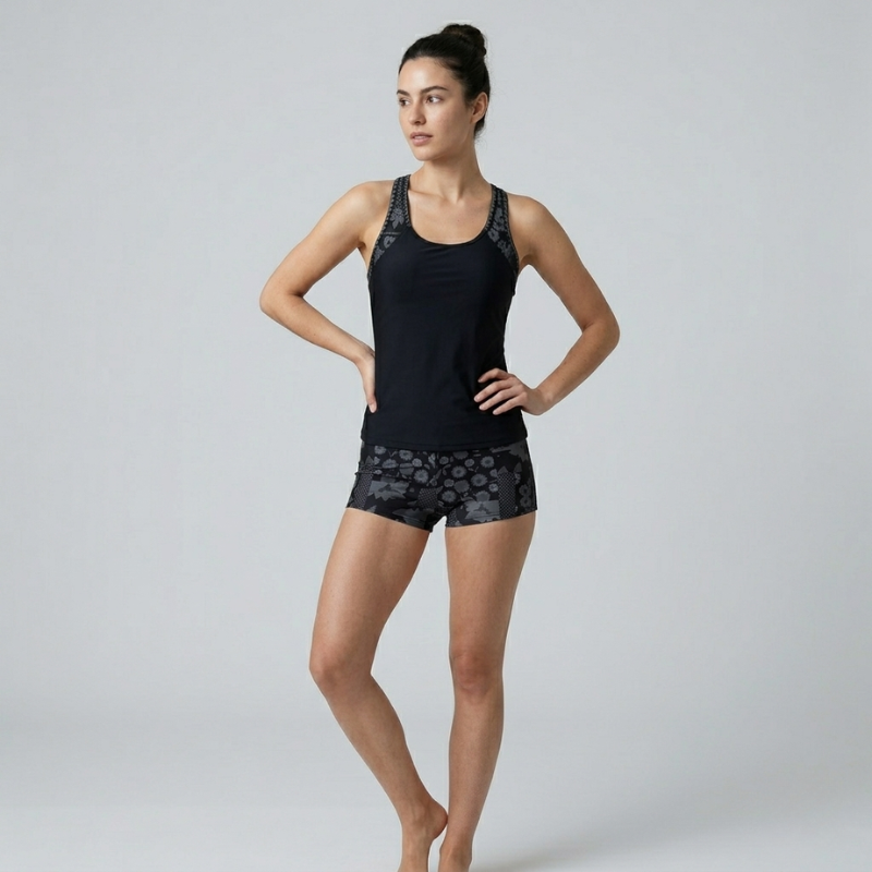 Front view of a black racerback tankini top and patterned boy shorts on a female model.