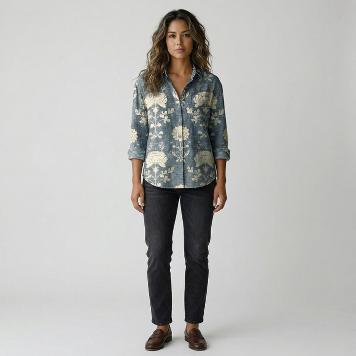 Woman wearing a blue button-down shirt with a large botanical leaf pattern and black trousers.