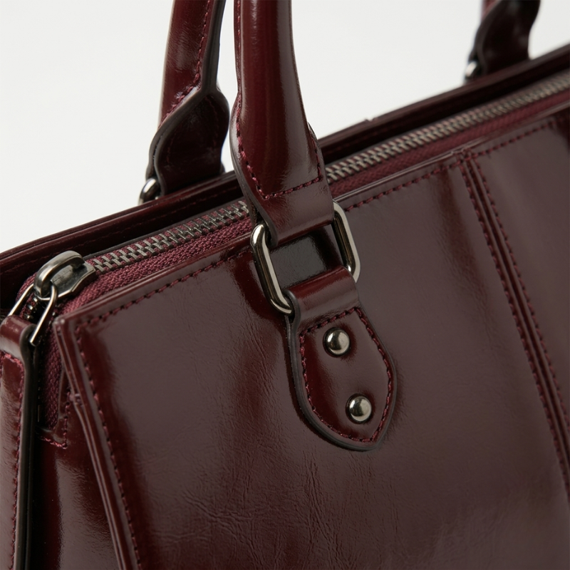 Close-up of a maroon handbag with a handle and zipper on a light gray background