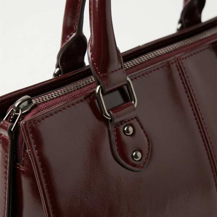 Close-up of a maroon handbag with a handle and zipper on a light gray background