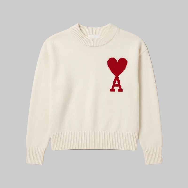 High-quality studio shot of a cream crewneck sweater featuring a red heart and letter logo on the chest.