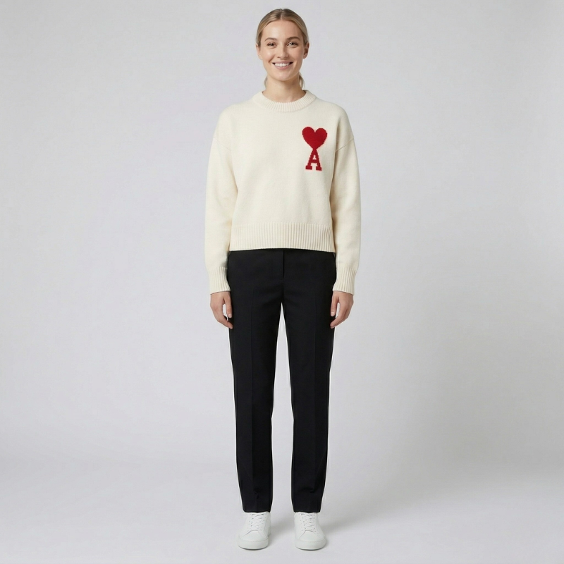 Minimalist studio shot of a cream-colored sweater with a red heart logo paired with black trousers.