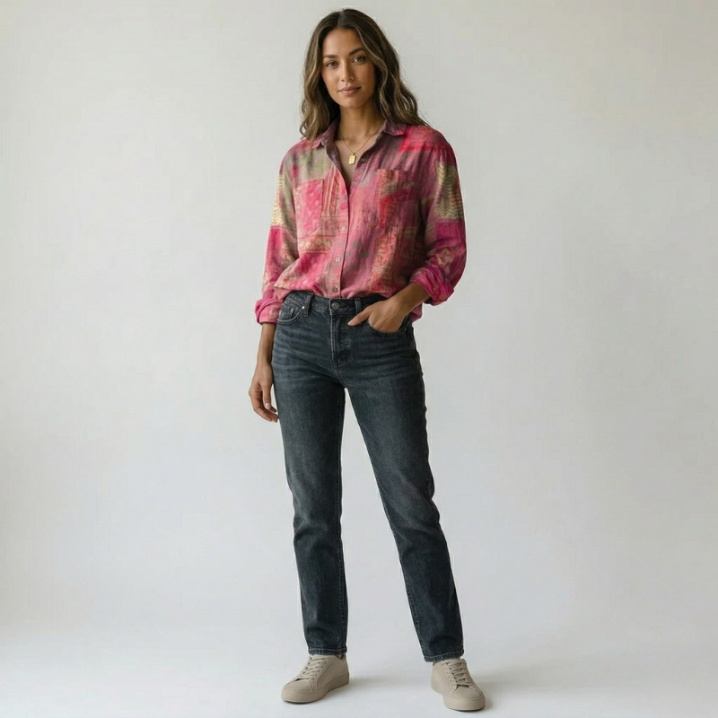 Model posing in a pink patterned long-sleeve blouse tucked into dark slim-fit jeans.