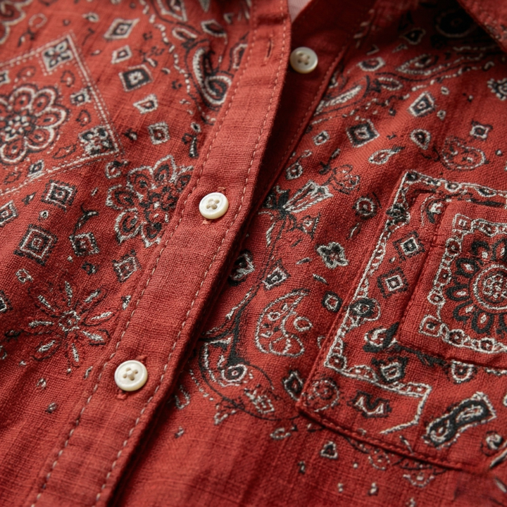 Close-up of the fabric, white buttons, and dark floral embroidery on a rust red cotton shirt.