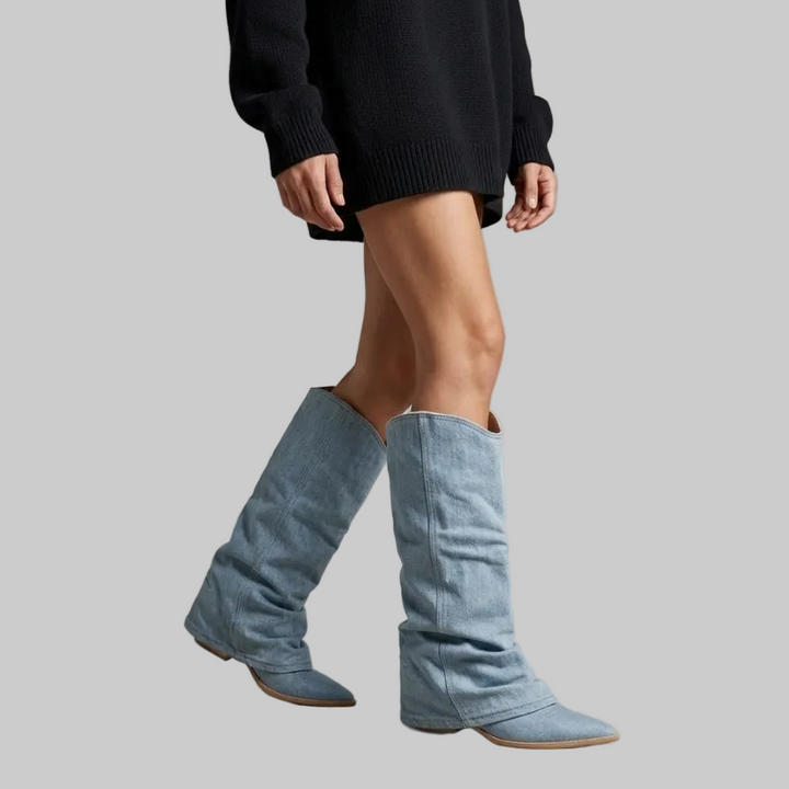 Person wearing blue knee-high boots with a plain background